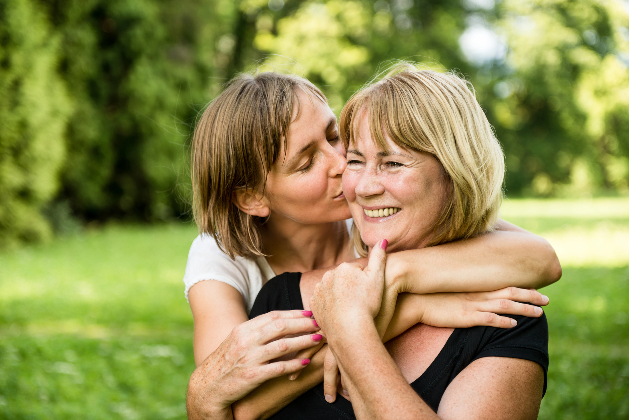 An adult daughter embracing her aging mother outdoors